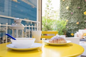 A yellow table with a white ceramic cup, a white ceramic bowl, and a plate with a pastry. - La Casa di Luna BnB (Naples)
