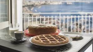 Una mesa con un pastel, gofres, un vaso de leche y una taza, con vistas panorámicas a la costa a través de una ventana.