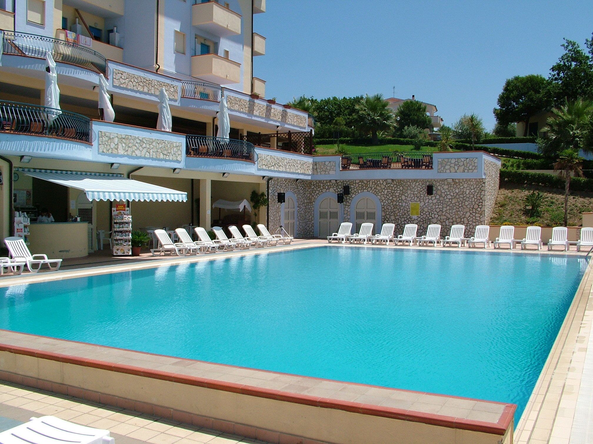 A swimming pool with white lounge chairs and a stone building with balconies.
