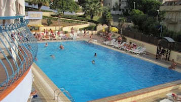 Une piscine où des gens nagent et prennent des bains de soleil. Des chaises longues et des parasols sont disposés autour de la piscine.