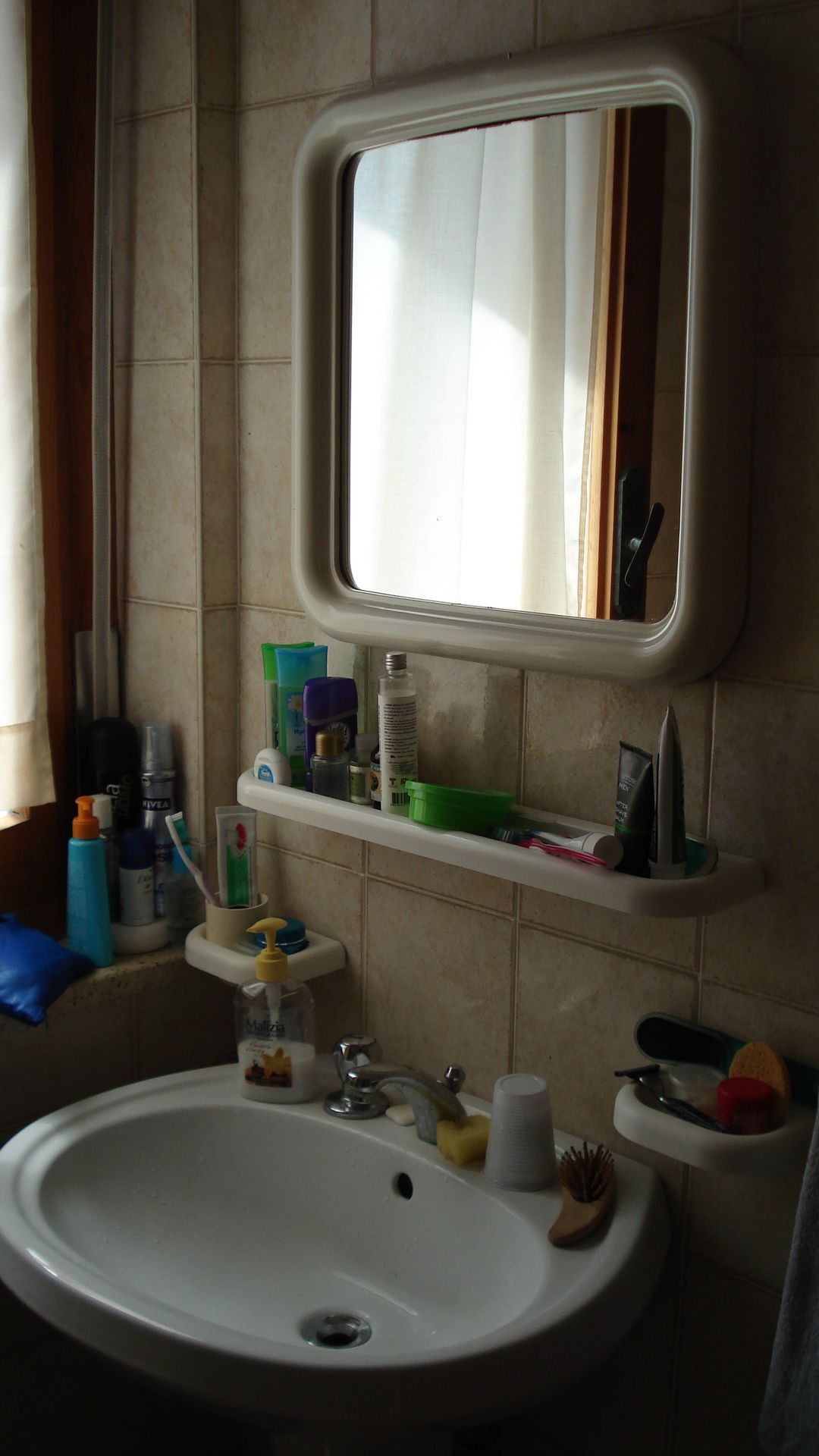 A bathroom with a white sink, a mirror above it, and a shelf with toiletries.