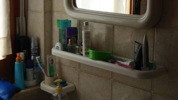 A bathroom with a white sink, a mirror above it, and a shelf with toiletries.