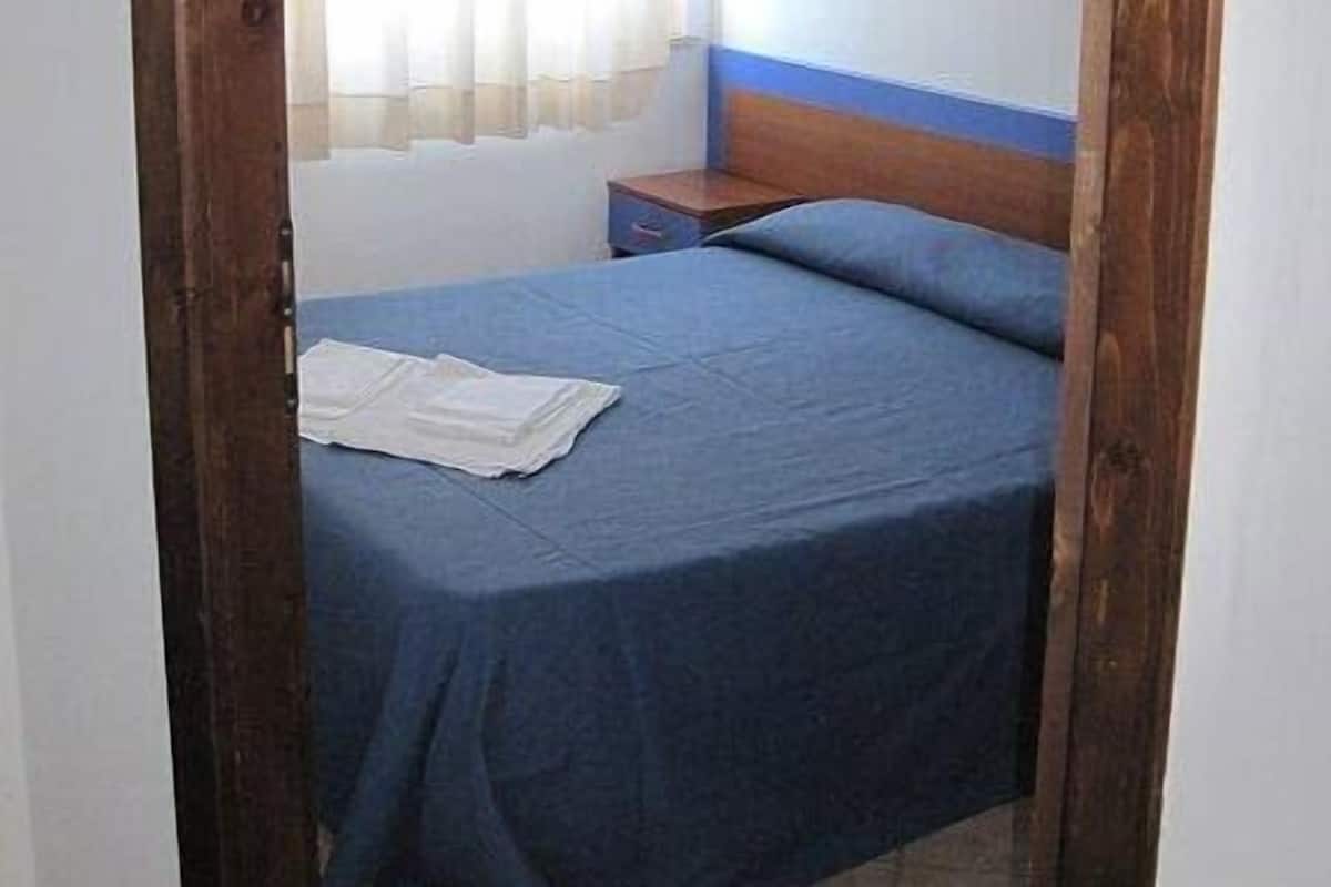 Une petite pièce simple, avec un lit, une table de chevet et une fenêtre avec des rideaux.