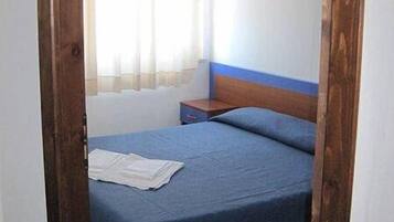 A small, simple room with a bed, a nightstand, and a window with curtains.