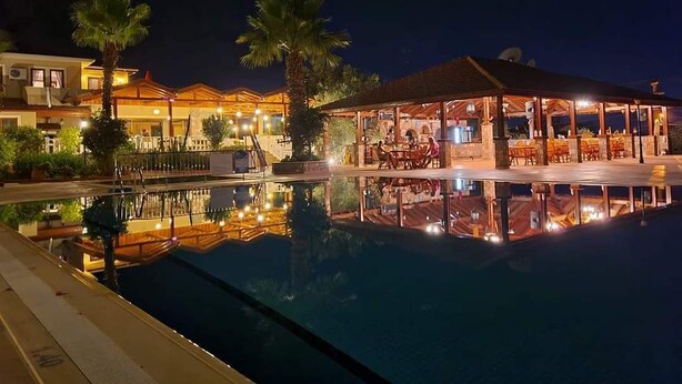 Vista nocturna de un hotel con piscina, mobiliario exterior y palmeras.