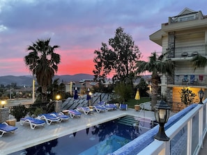 A poolside area with lounge chairs, a pool, and a building with balconies. - Celay Hotel (Fethiye)
