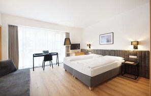 A modern hotel room with a large bed, a desk, a chair, and a sofa. - Hotel Goldene Rose (Brunico)