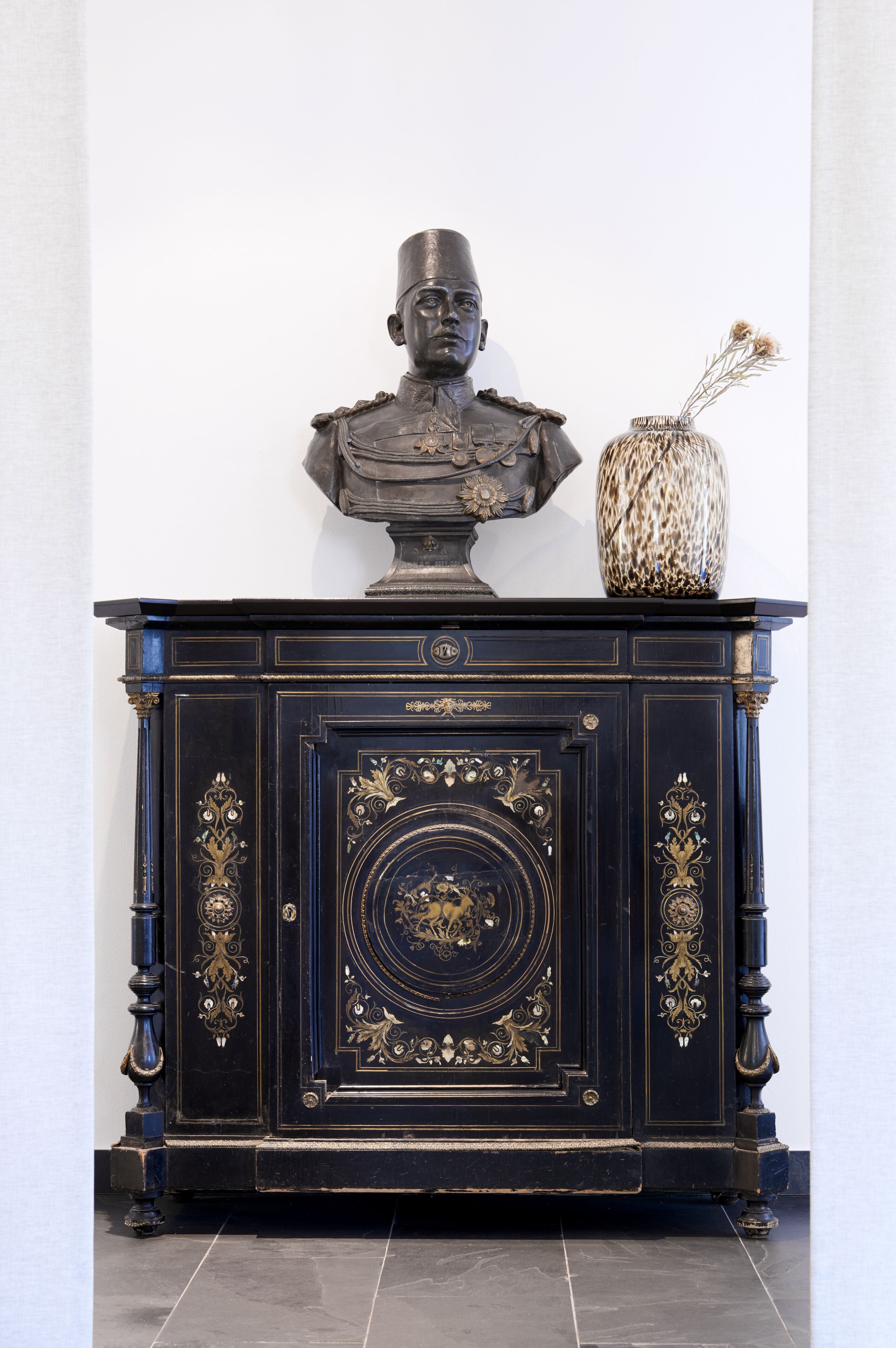 Eine schwarze, kunstvoll verzierte Kabine mit einer Büsten-Skulptur und einer Ziervase.