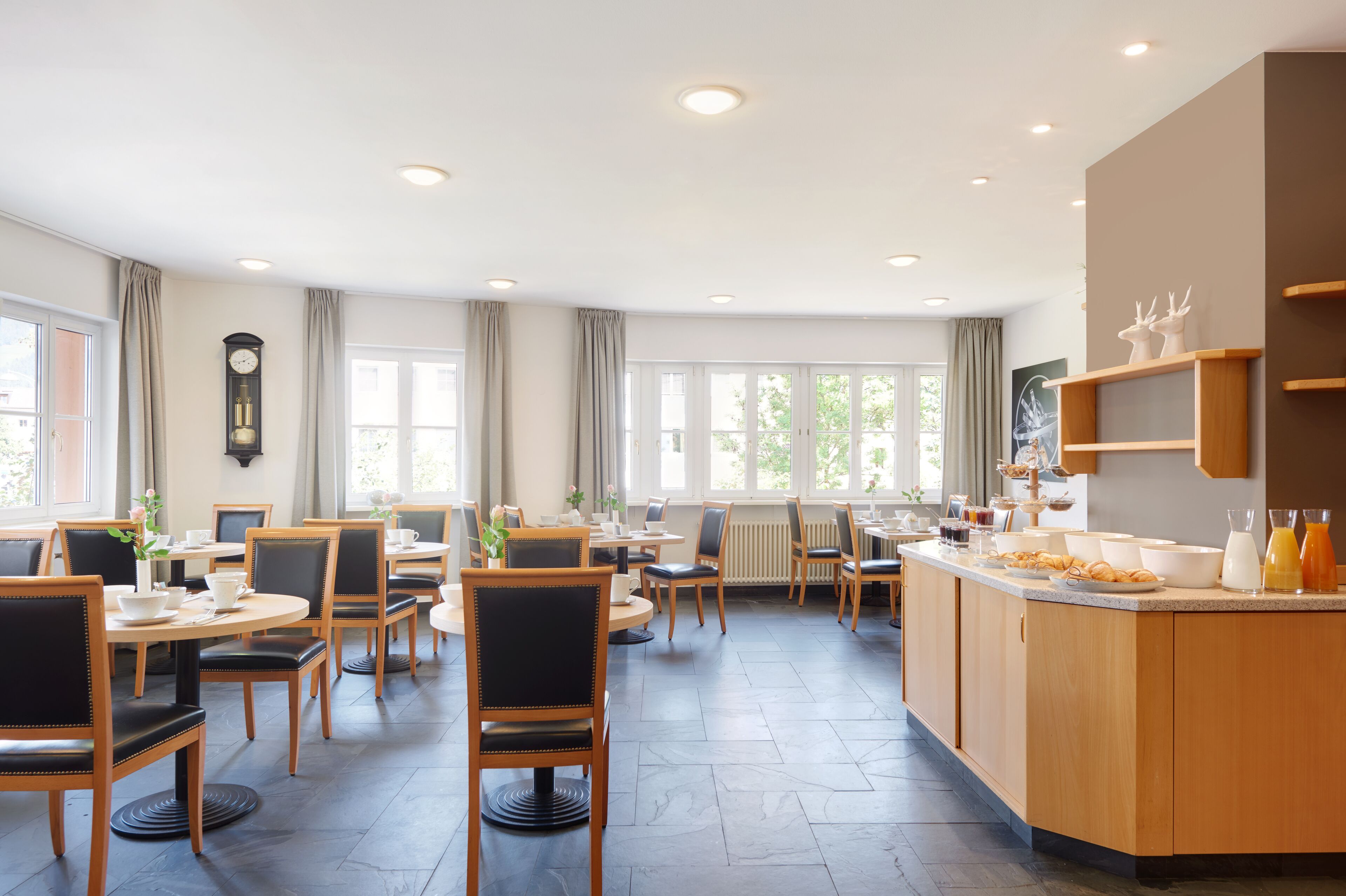 A dining area with round tables and chairs, a buffet counter with food and drinks, and a clock on the wall.