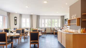 A dining area with round tables and chairs, a buffet counter with food and drinks, and a clock on the wall.
