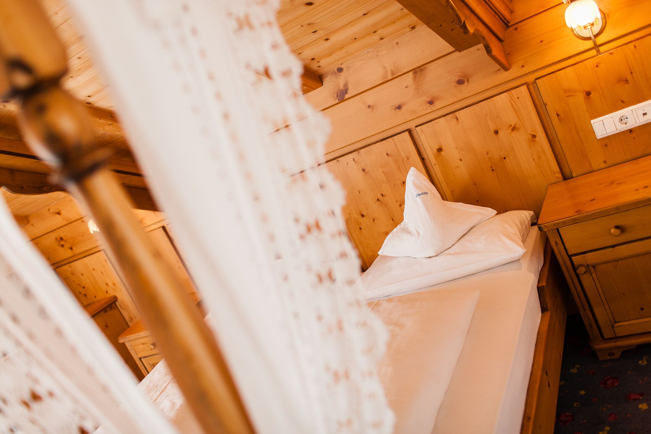 Una habitación tipo cabaña de madera con una cama, una mesita de noche y una lámpara fijada a la pared.