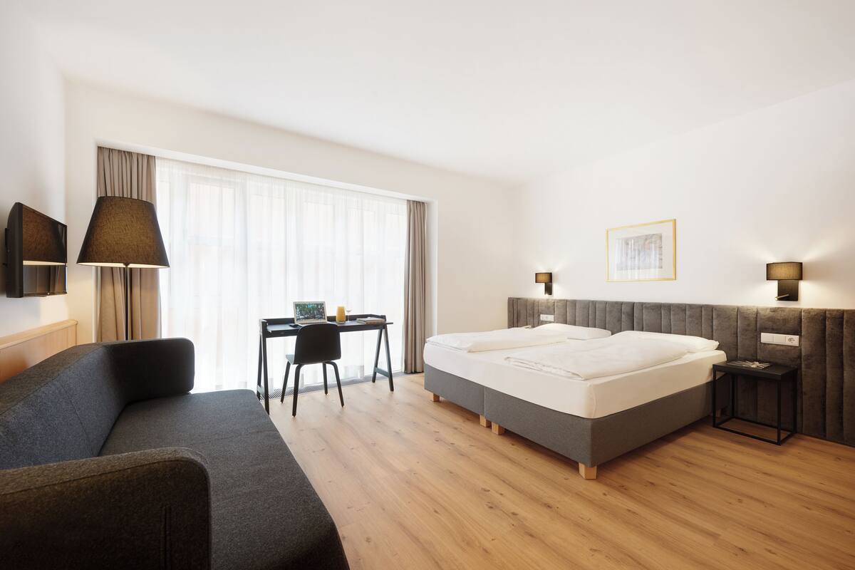 A modern hotel room with a large bed, a desk with a chair, and a TV mounted on the wall.