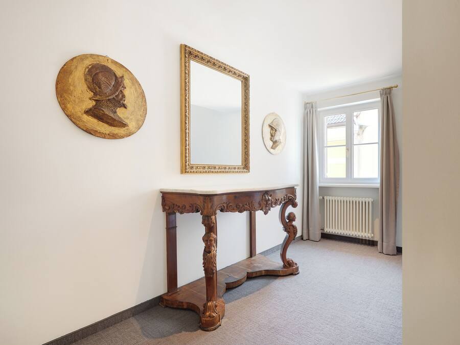A hallway with a wooden console table, a large mirror, and two decorative wall pieces.