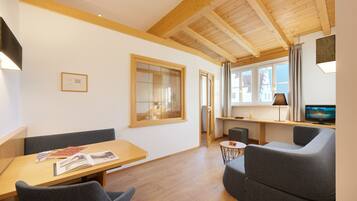 Ein modernes Wohnzimmer mit Holzboden, einem Essbereich mit Tisch und Stühlen, einer Couch und einem Fernseher.