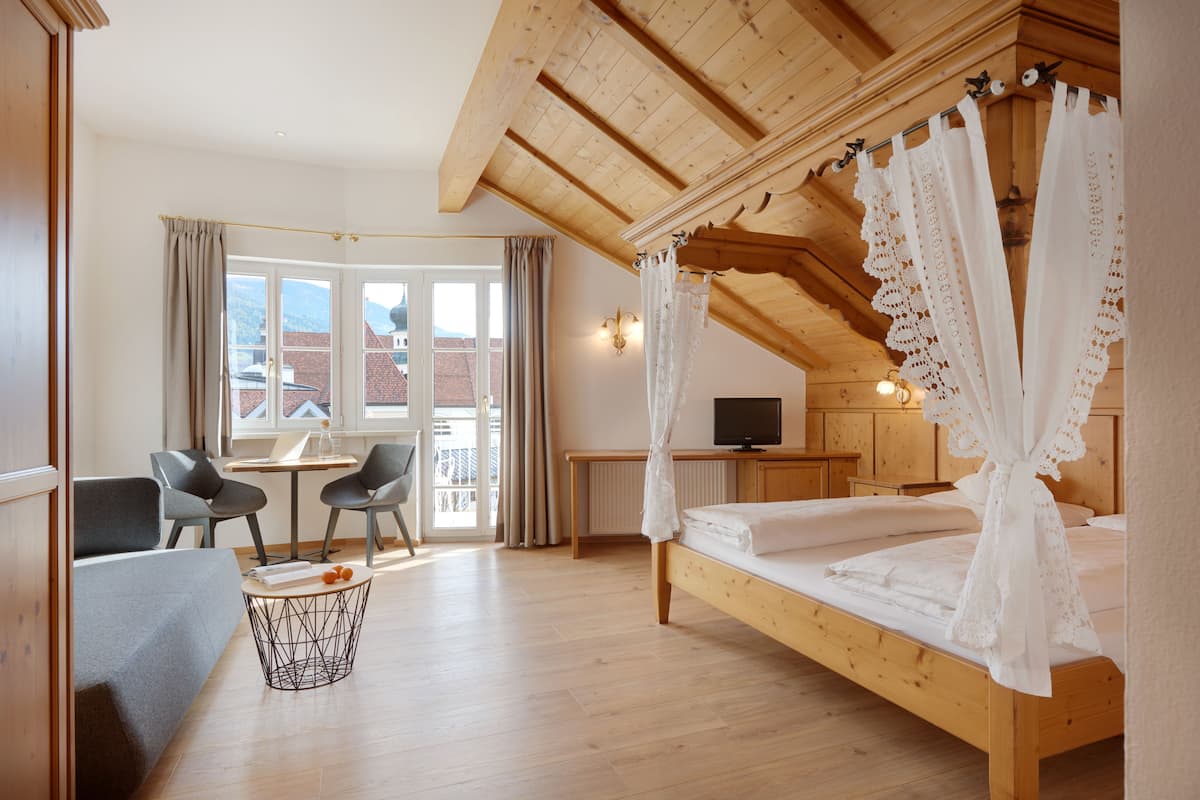 A bedroom with a wooden ceiling, a bed with a canopy, a desk with a chair, and a view of the outside.
