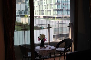 Een balkon met een tafel en stoelen, een bloevas en uitzicht op een modern gebouw.