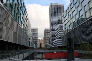 Een modern complex van stadsgebouwen met meerdere hoge torens, een voetgangersbrug in het midden en een heldere lucht.