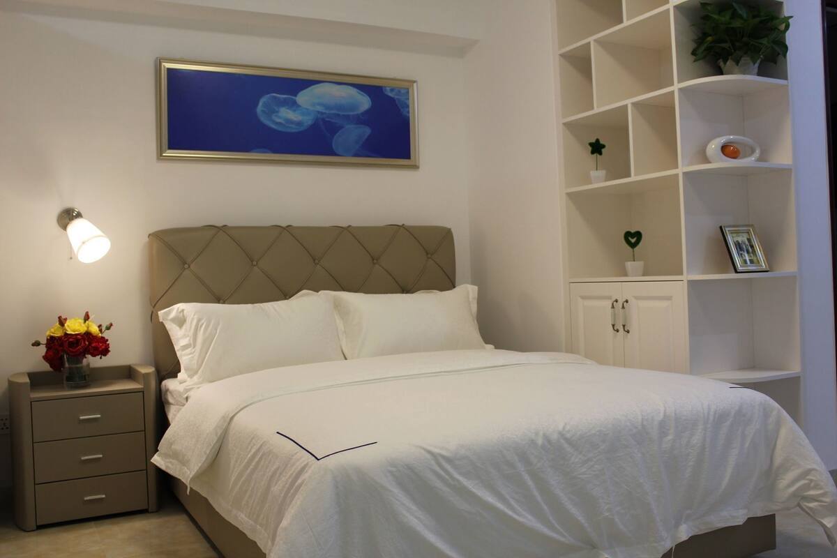 A neatly made bed with a headboard, a bedside table with a lamp, and a wall-mounted shelf with decorative items.