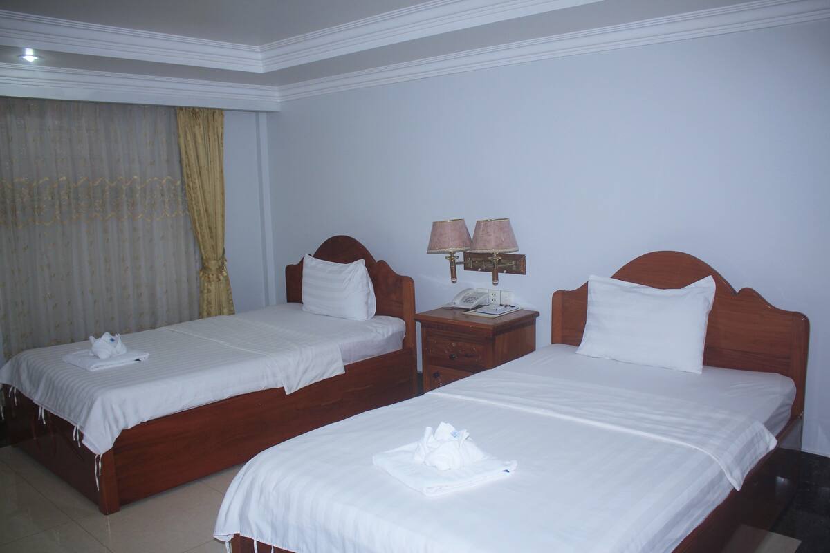 A hotel room with two single beds, a nightstand with a lamp, and a telephone.