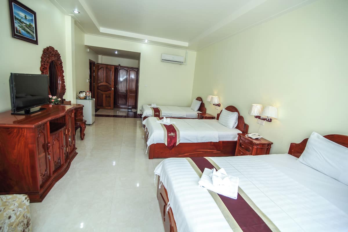 A hotel room with two beds, a TV, a wooden cabinet, and a desk with a lamp.