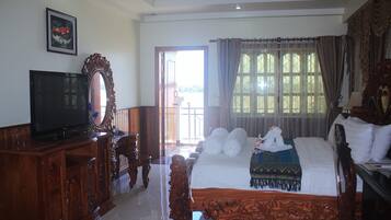 A bedroom with a large bed, a wooden dresser, a television, and a window with curtains.