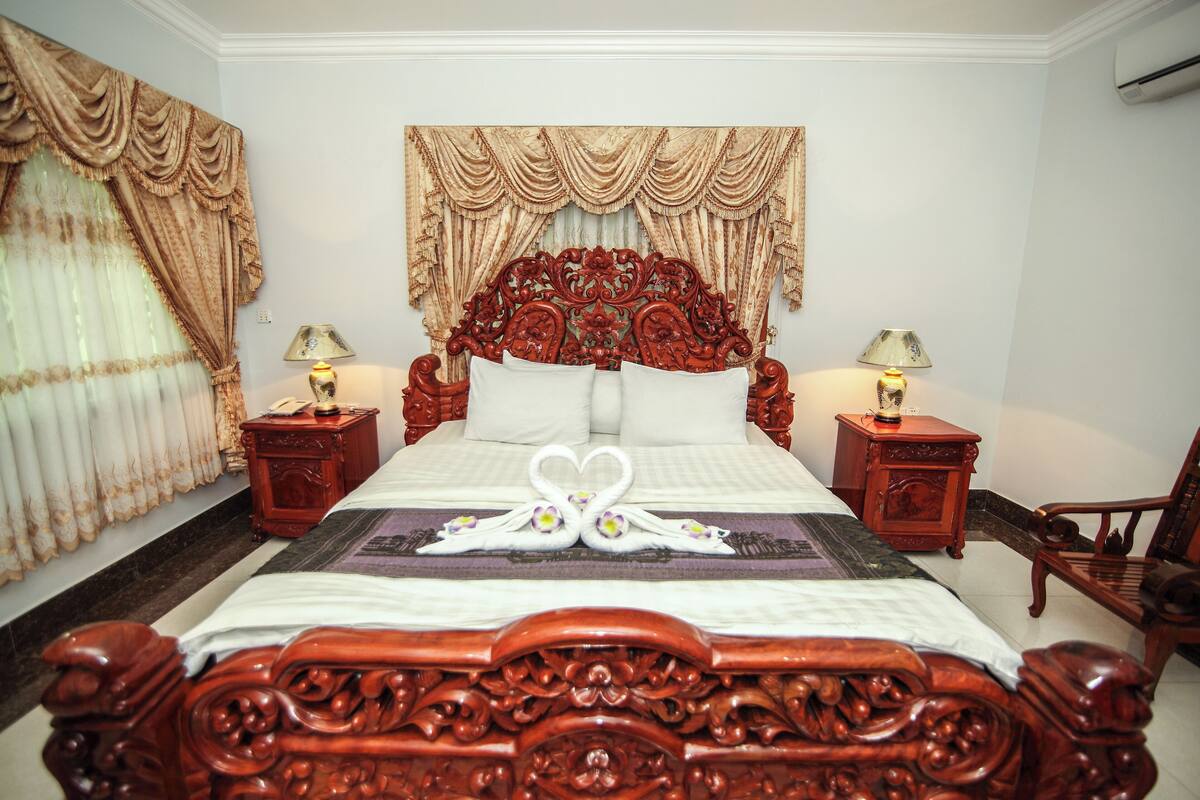 A large, ornate bed with a heart-shaped swan decoration, two nightstands with lamps, and a chair.