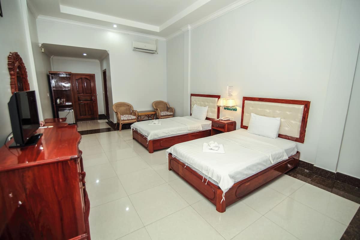 A hotel room with two beds, a desk with a computer, a chair, and a wardrobe.