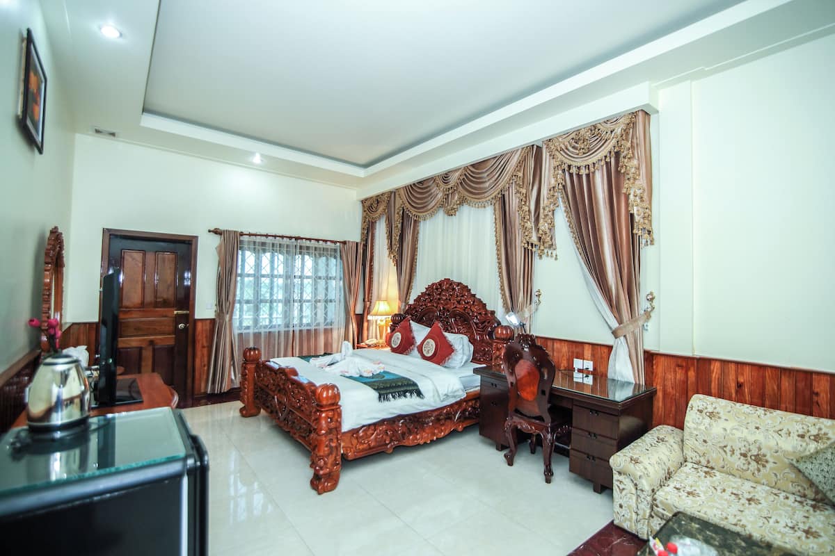 A spacious hotel room with a large bed, a wooden desk, a sofa, and a television.