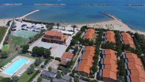 Una vista aerea di un resort costiero con piscina, spiaggia e diversi edifici con tetti in tegole rosse.