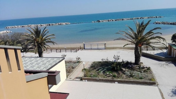 Vista de una playa con palmeras, arena y un rompeolas rocoso.