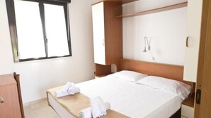 Una camera d'albergo con un letto, un armadio in legno, un comodino e una finestra con tende.