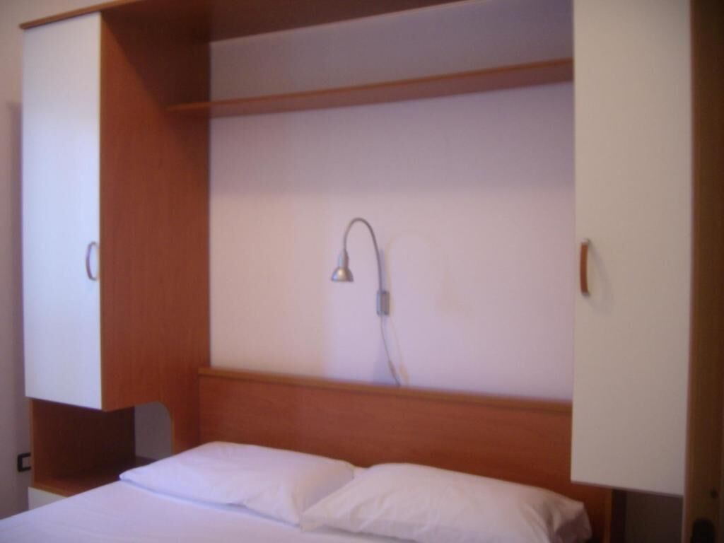 Une chambre à coucher avec une tête de lit en bois, un lit avec une literie blanche et une lampe fixée au mur.
