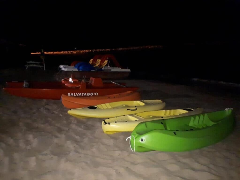 Several kayaks lined up on a sandy surface at night.