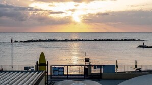 Vista sulla costa con tramonto, un molo, e una spiaggia con una torretta di salvataggio e una tavola da surf.