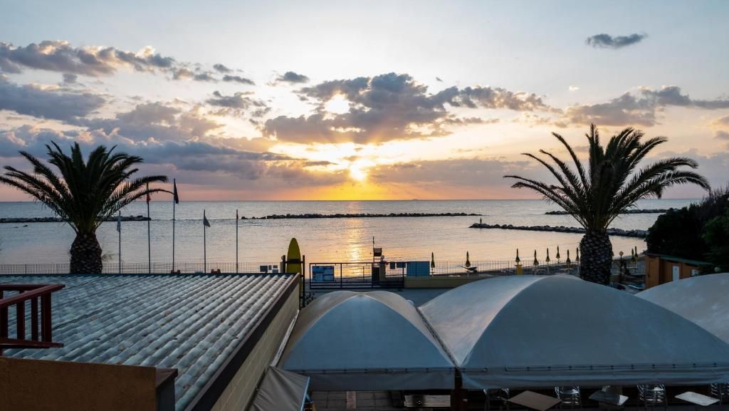 A coastal view with a sunset, palm trees, and a pier extending into the water.