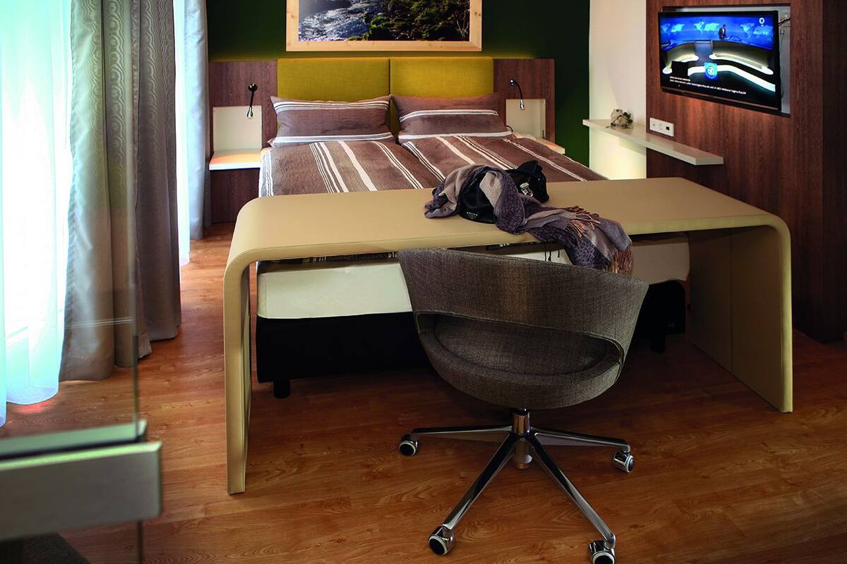 A hotel room with a bed, a desk, a chair, a television, and a window with curtains.