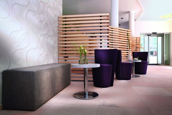 Ein stilvoller Lounge-Bereich mit einer grauen gepolsterten Bank, einem runden Tisch mit Blumenvase und violetten Polstersesseln.