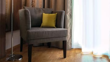 Un sillón gris con un cojín amarillo en una habitación con suelo de madera y cortinas.