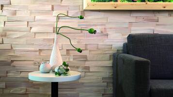 Ein modernes Interieur mit einer Holzwand, einem runden Tisch mit einer Vase und Dekorationselementen sowie einem grauen Sessel.