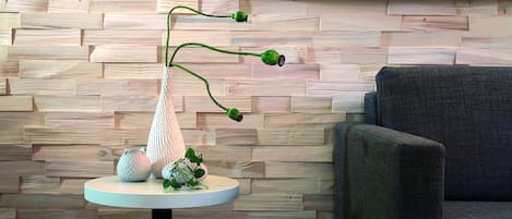 Un interior moderno con una pared de madera, una mesa redonda con un florero y objetos decorativos, y un sillón gris.