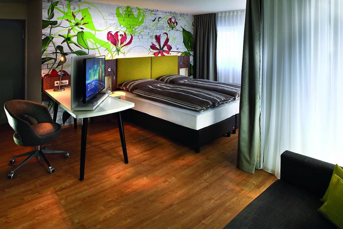 A modern hotel room with a bed, desk, chair, and a large window with curtains.
