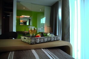 Habitación de hotel con zona de comedor que incluye una mesa con una bandeja de mimbre que contiene dos copas de vino, una manzana y una flor.
