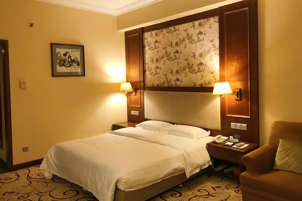 A hotel room with a large bed, two bedside lamps, a nightstand with a phone, and a chair.