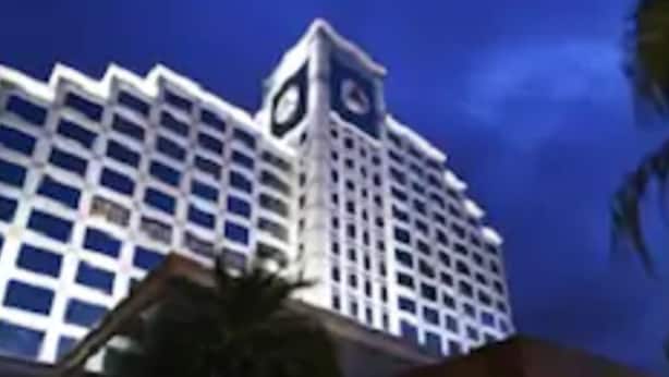 Un hotel grande con una imponente torre de reloj, una entrada bien iluminada y una zona ajardinada con palmeras.
