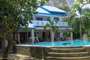 A two-story building with a swimming pool, outdoor seating, and a stone staircase leading to the pool.