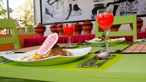 A dining table with plates of food, a glass of red drink, and a painting in the background. - Ariyana Wellness Retreat Yala (Thissamaharama)