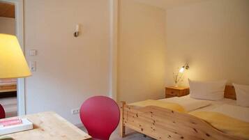 Ein Schlafzimmer mit einem hölzernen Bett, einem Nachttisch mit Lampe, einem roten Sessel und einem weiteren kleinen Nachttisch mit einer Pflanze.