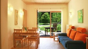 A cozy living room with a sofa, a dining table with chairs, and a view of a garden through a sliding door. - Biohotel Spöktal (Bispingen)