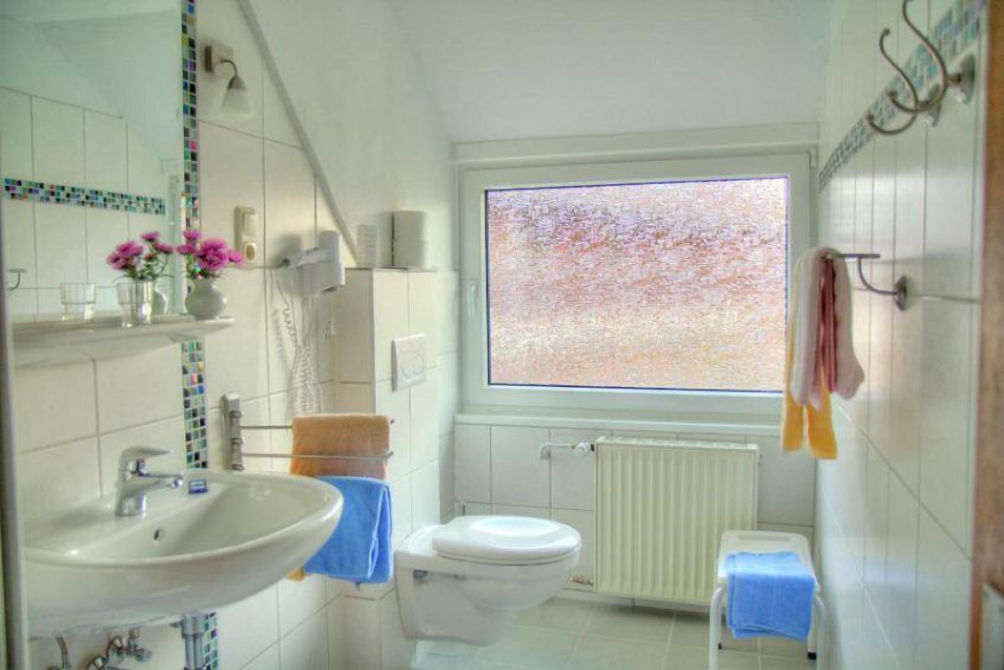 A bathroom with a white sink, a toilet, a window with a view, and a radiator.