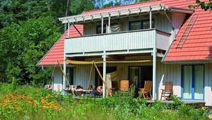 A two-story house with a red roof, a balcony, and a covered porch with chairs. - Biohotel Spöktal (Bispingen)